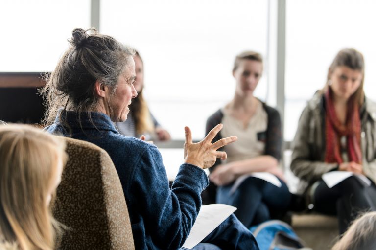 Instructor sitting in a circle of chairs talking to a group of university students.