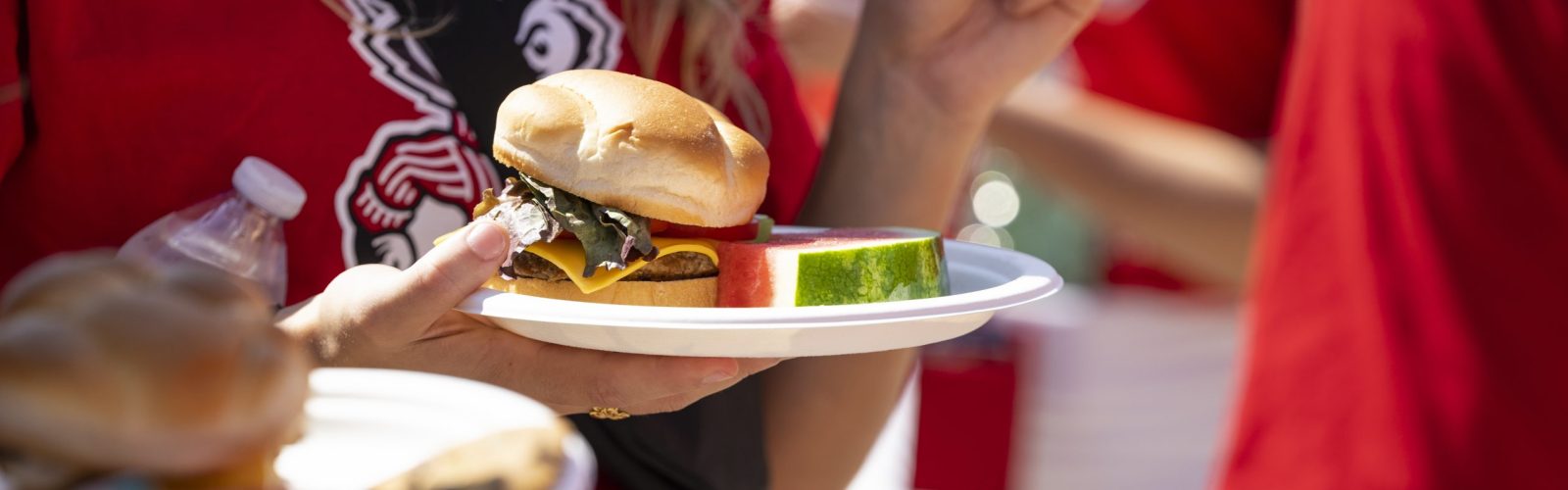 Person in red UW shirt holding a plate with a burger and watermelon slice
