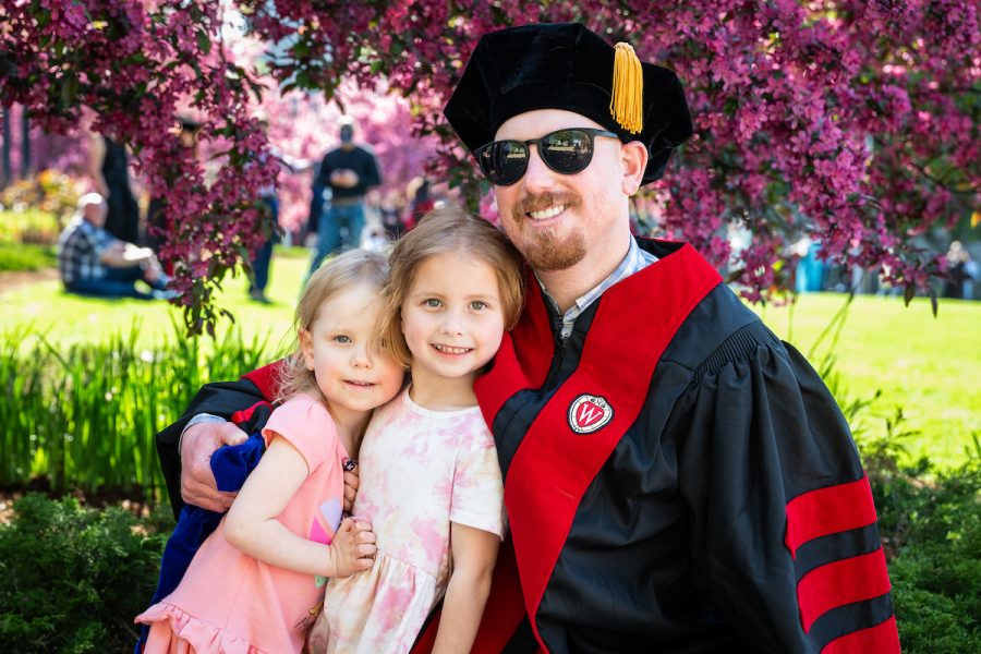 A graduate hugging his two daughters.