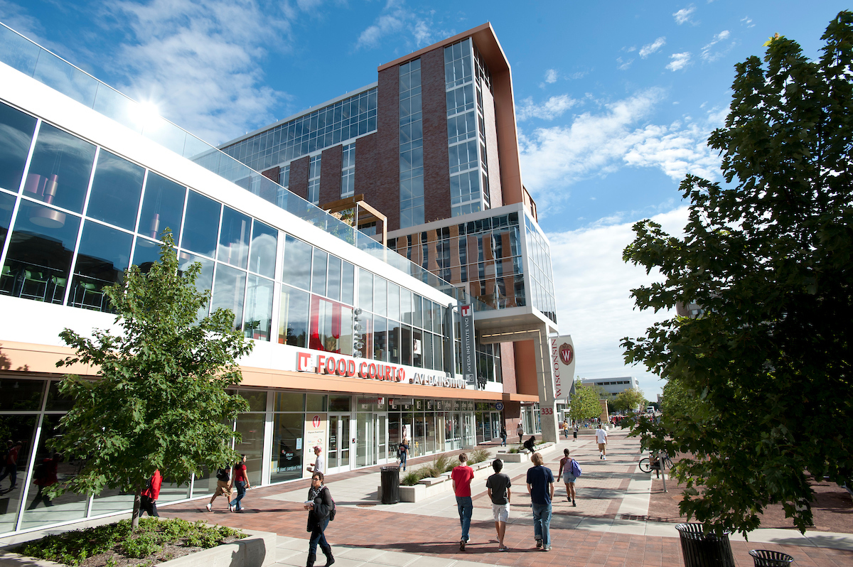 Pedestrians walk past the University Square complex and Student Services Tower on a sunny day.