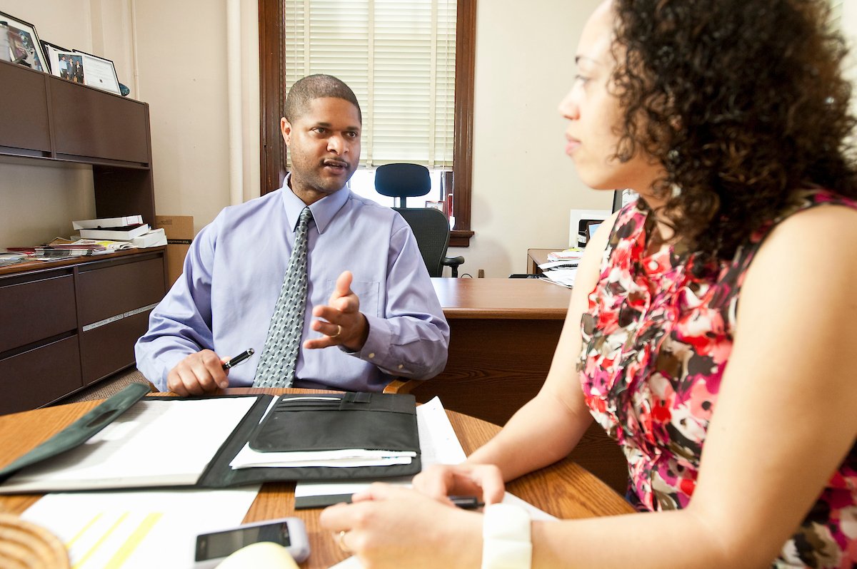 Assistant dean talking at his desk with a female graduate student.