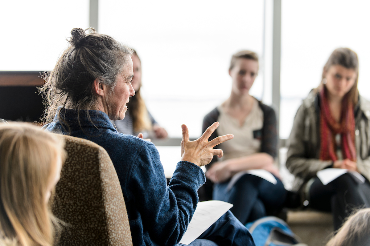 Instructor sitting in a circle of chairs talking to a group of university students.