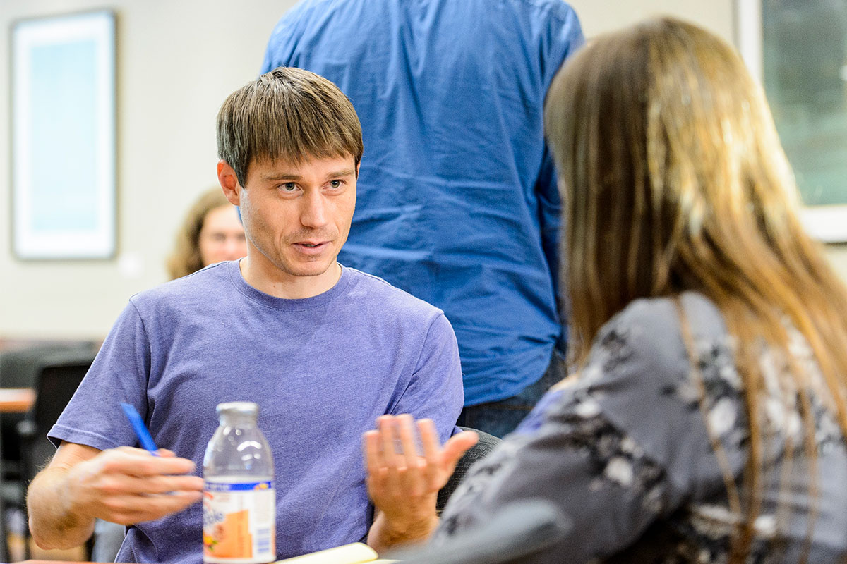 two seated individuals having a conversation, another individual standing in the background