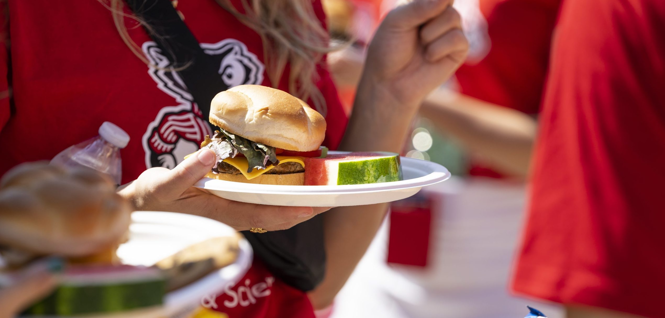 Person in red UW shirt holding a plate with a burger and watermelon slice